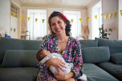 Eine lachende Hebamme mit einem Neugeborenen nach der Hausgeburt Baby im Arm.