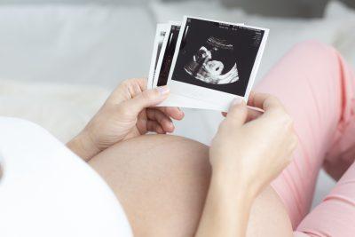 Eine schwangere Frau liegt und betrachtet ihre Ultraschallbilder.