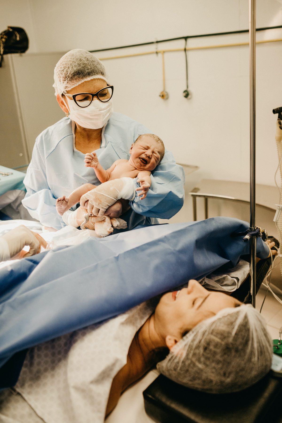 Eine Mutter direkt nach einem Kaiserschnitt und eine Krankenschwester, die gerade das Neugeborene in der Hand hält.