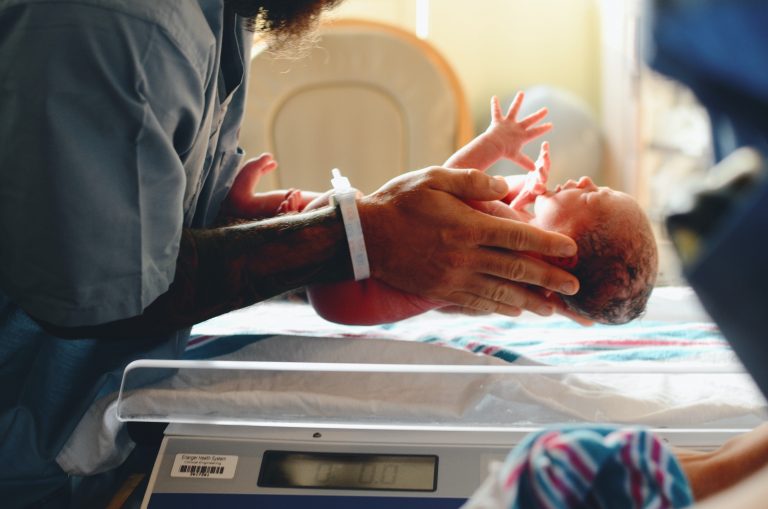 Eine Krankenschwester, die ein Neugeborenes nach der Geburt im Krankenhaus auf die Waage legt.