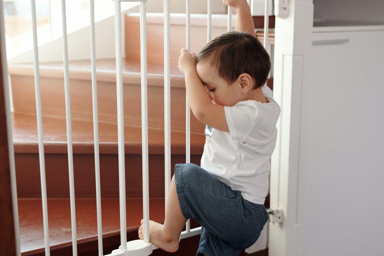 Ein Kleinkind versucht über das Kindergitter vor der Treppezu kelttern.