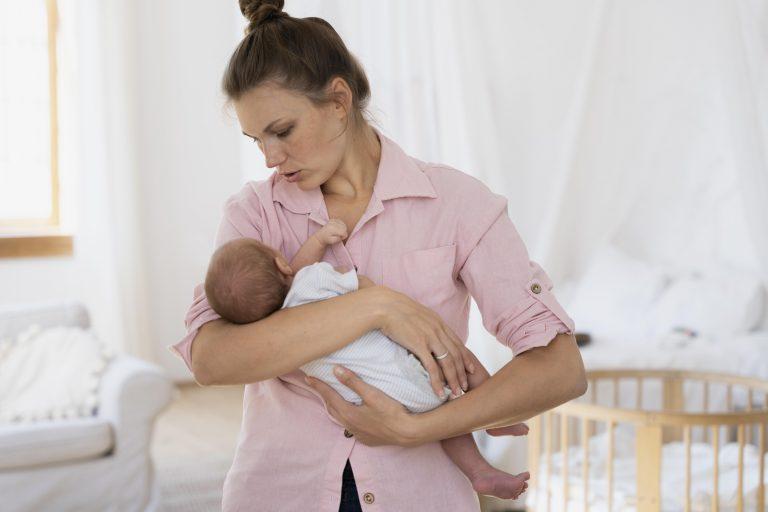 Mutter im Wochenbett hält Baby im Arm und blickt umkümmert auf das Kind