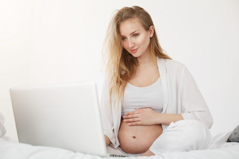 Schwangere Frau sitzt vor dem Laptop, um eine Beleghebamme zu finden