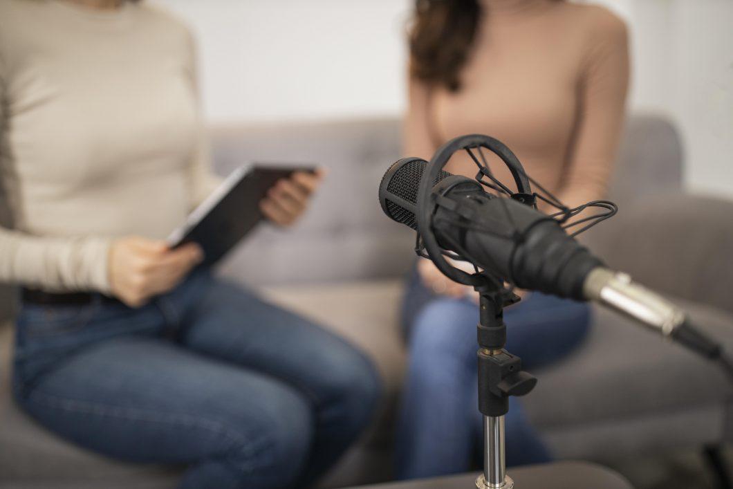 2 weibliche Personen sitzen vor Mikrofon und führen ein Interview durch.