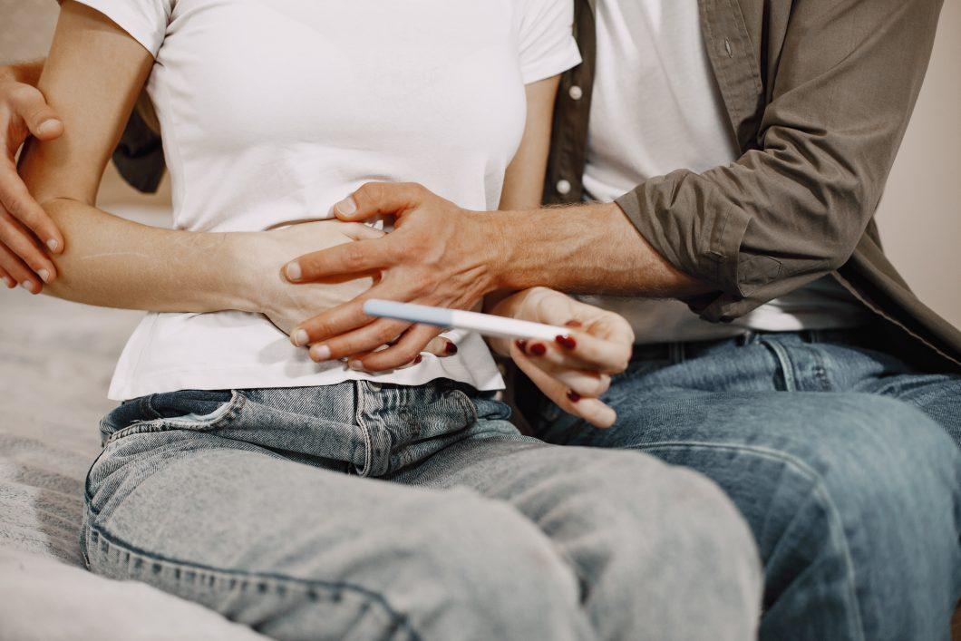 Paar hält den Bauch der schwangeren Frau und die Frau hält einen Schwangerschaftstest in der Hand.
