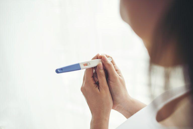 Frau hält in beiden Händen einen positiven Schwangerschaftstest